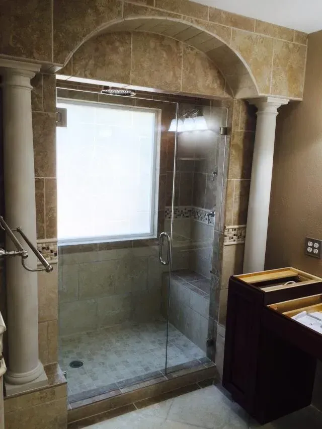 Bathroom with a tiled shower stall and glass door, featuring an arched top and decorative columns.