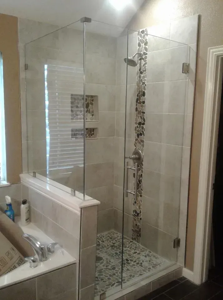Glass shower enclosure with stone floor and accent strip on tiled walls.
