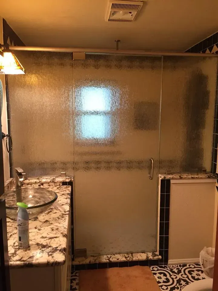 Bathroom with frosted glass shower door, vanity with a vessel sink, and black and white patterned tile.