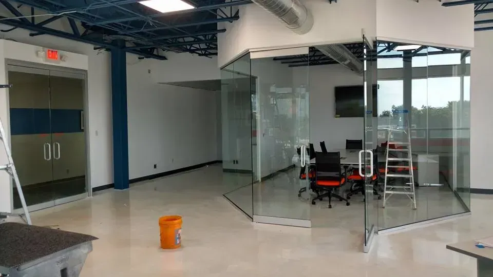 Modern office space interior with glass-walled conference room, orange chairs, and emergency exit.