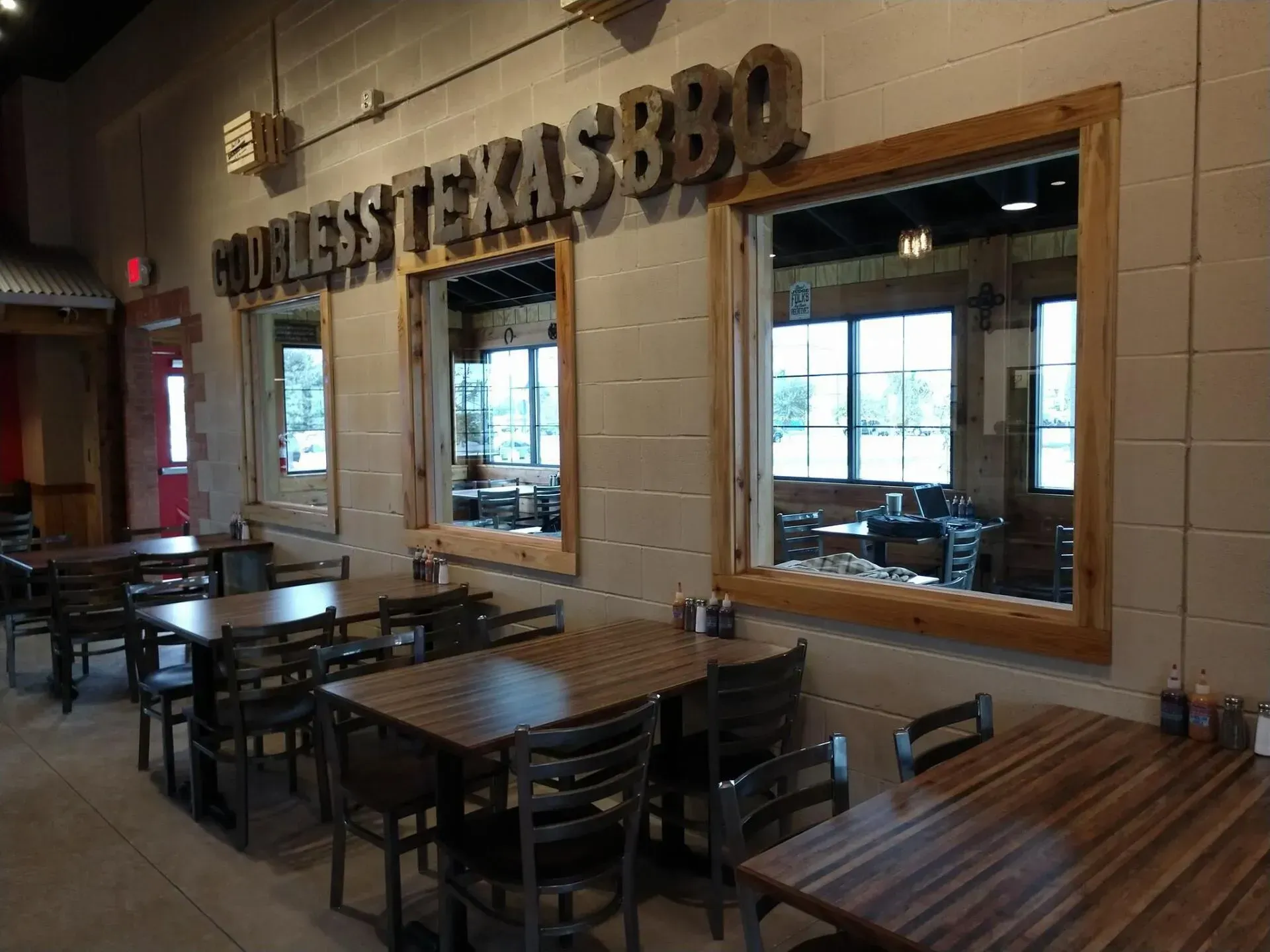 Interior of a BBQ restaurant with wooden tables and chairs, windows, and signage.