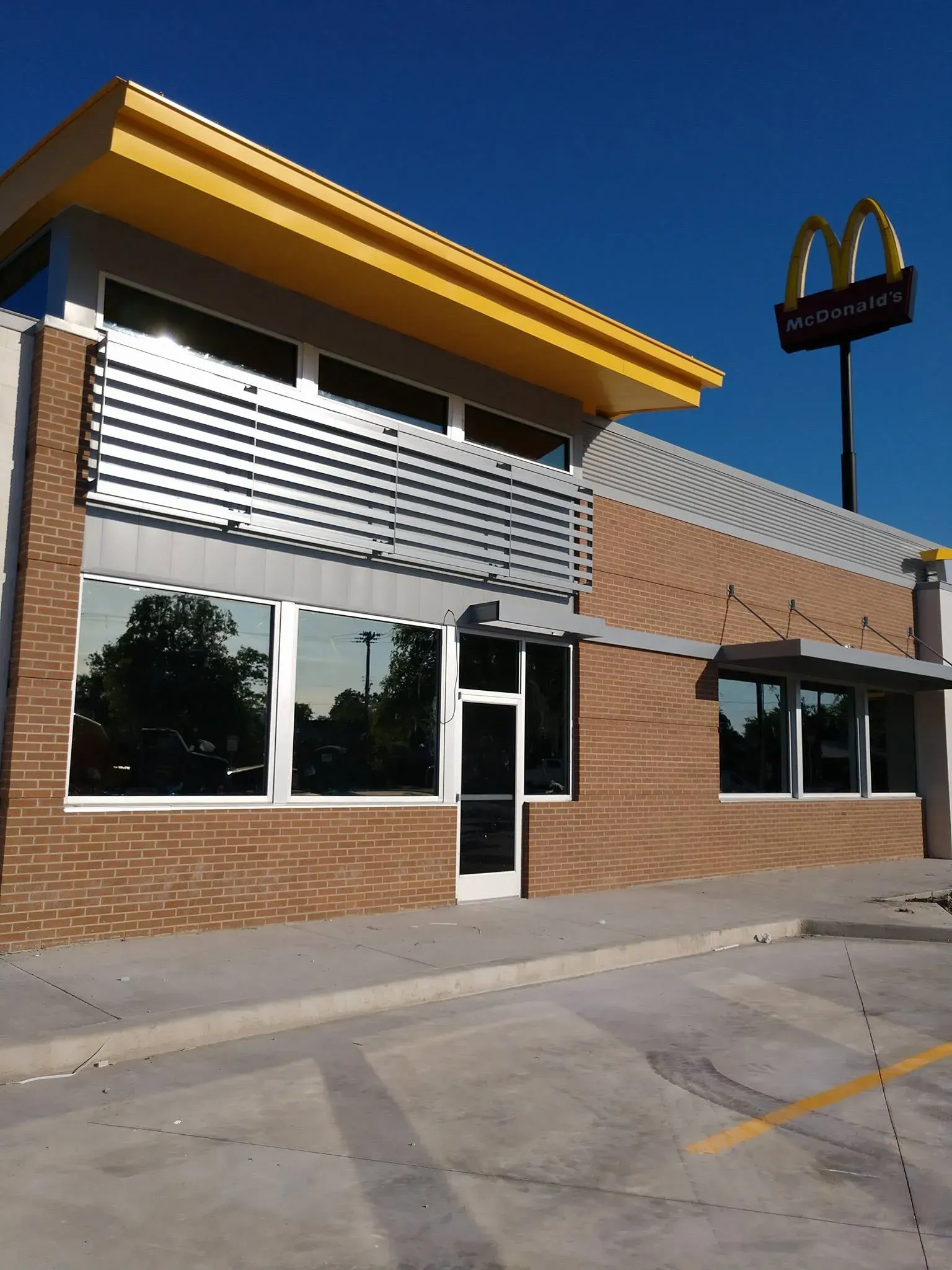McDonald's restaurant with yellow trim, brick facade, and a golden arch sign against a clear blue sky.
