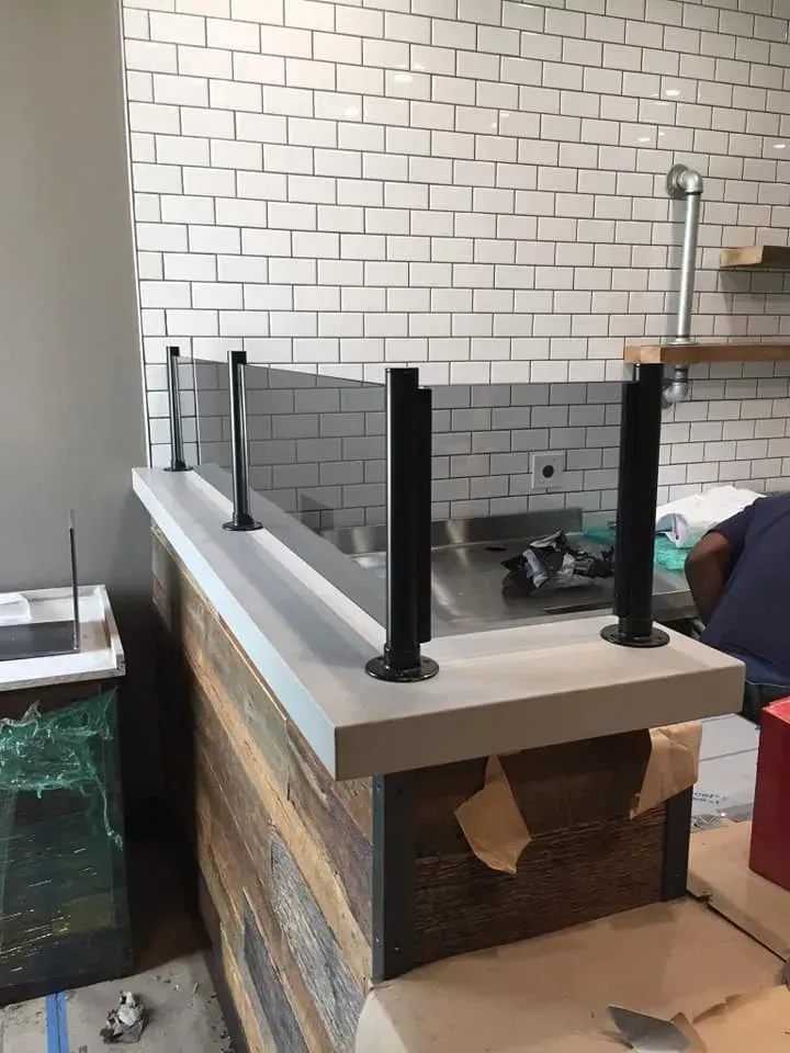 Counter with a clear glass barrier and black supports, set against a brick wall.