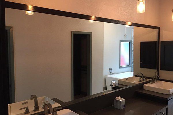 Bathroom with large mirror, two sinks, and overhead lighting. Dark frame around the mirror.