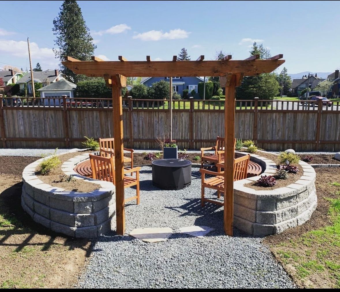 Outdoor fire pit area with wooden pergola, curved retaining walls, gravel path, and wooden benches.
