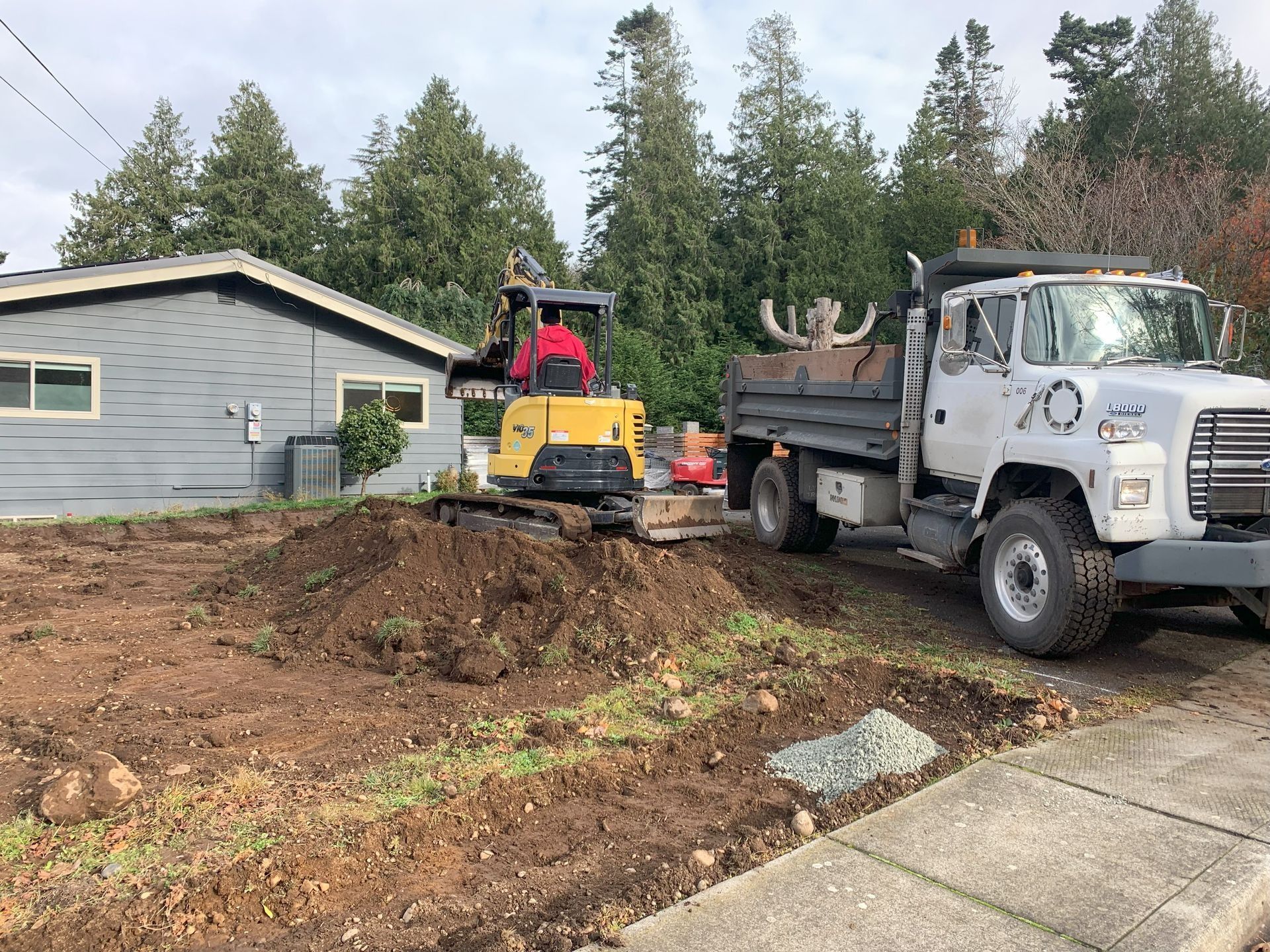 Construction site with a backhoe, dump truck, and a house.