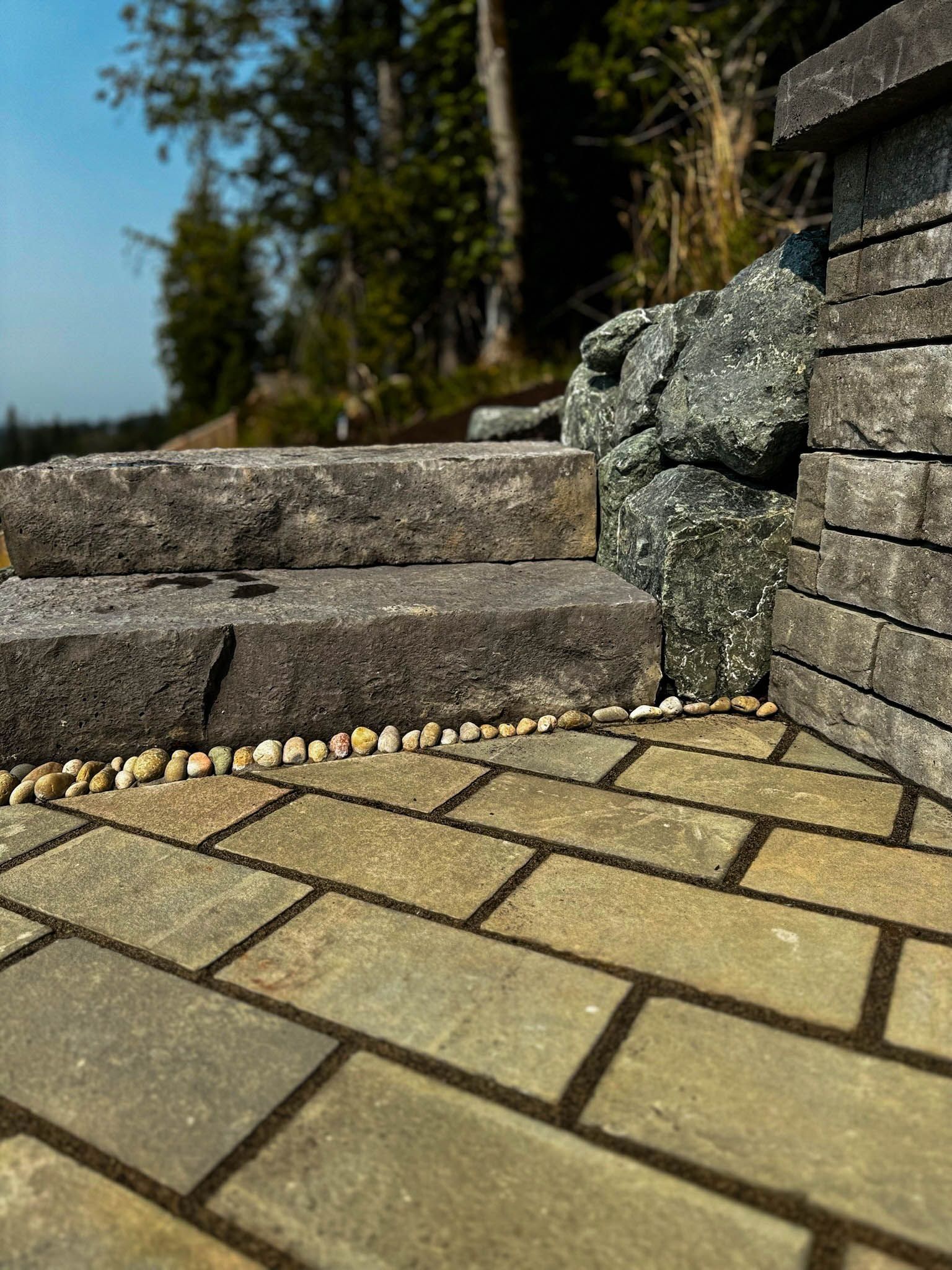 Stone steps leading up, next to a stone wall and brick patio, outdoors.