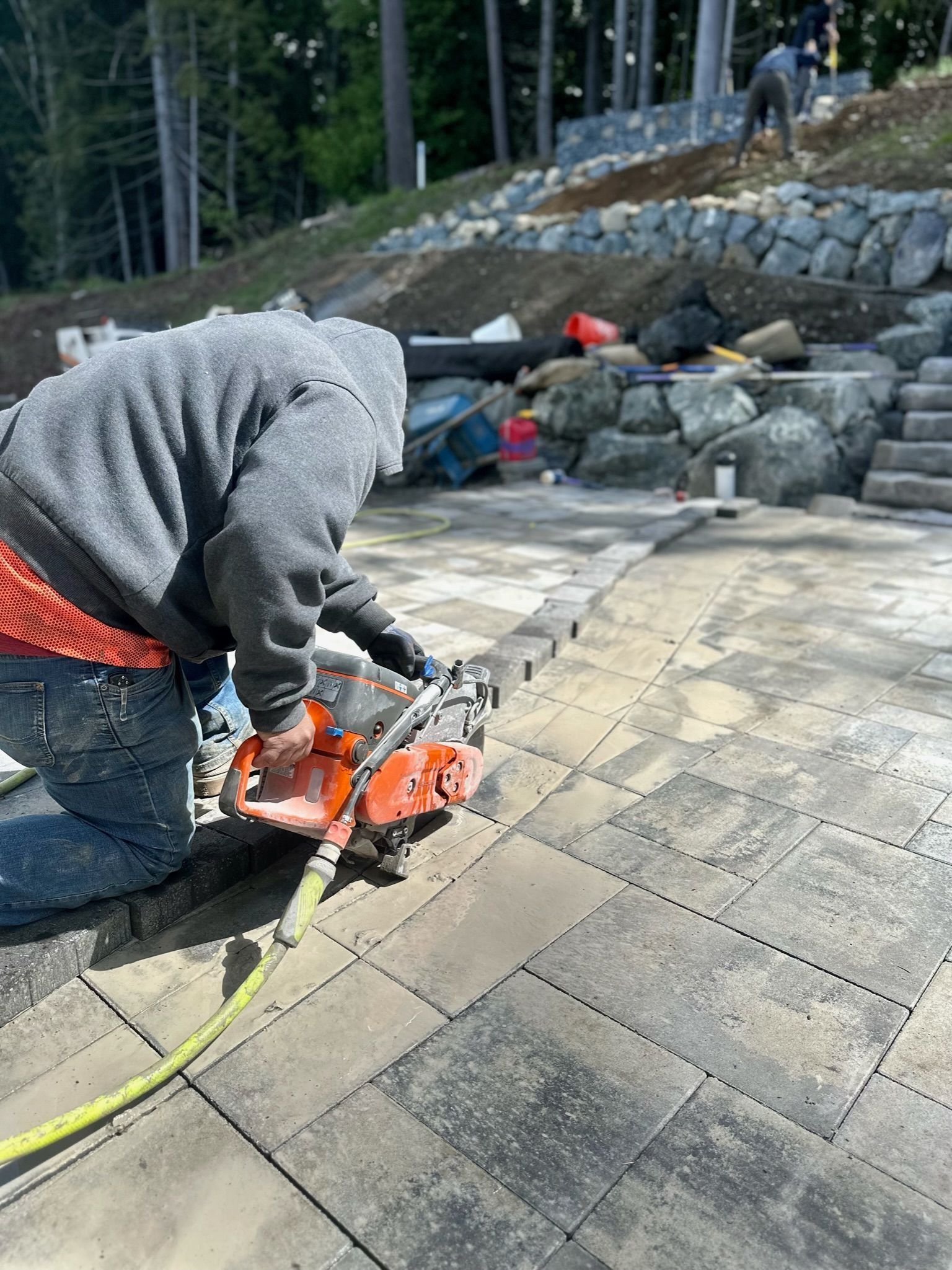 Person using a saw to cut paving stones, outdoor setting.