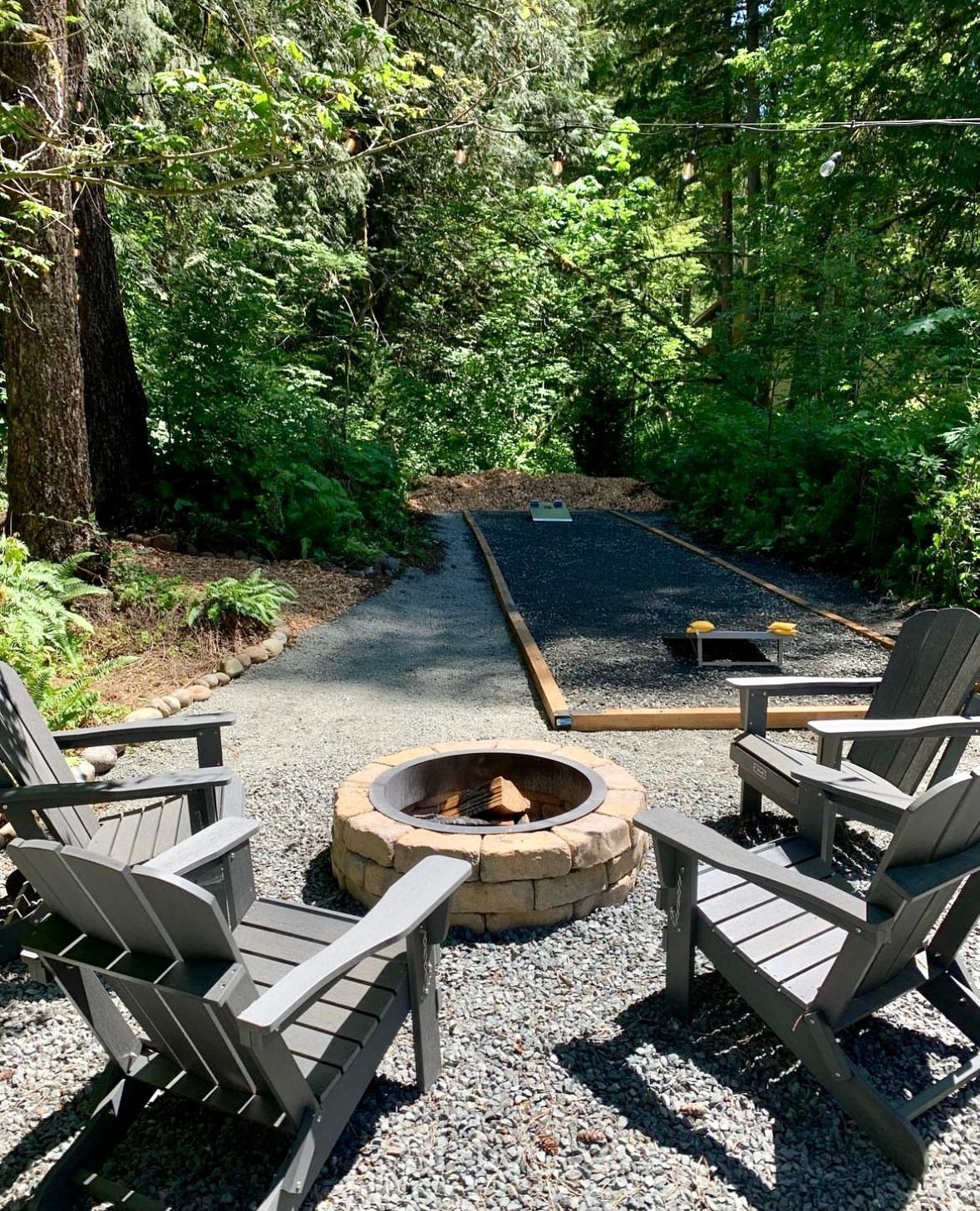 Outdoor scene with Adirondack chairs around a fire pit and a shuffleboard court.