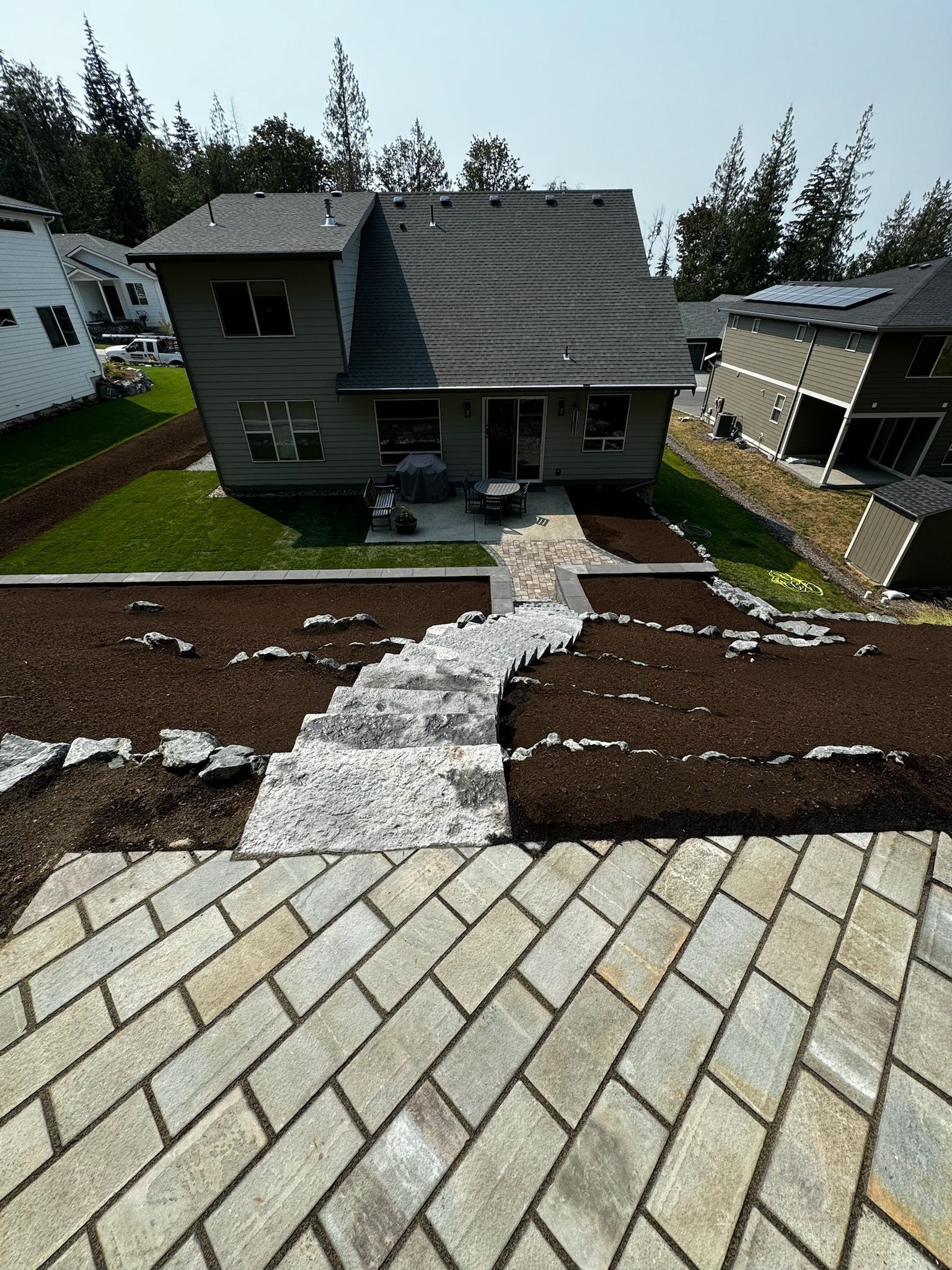 Stone path leads to a gray house with a dark gray roof. Steps and landscaped beds with mulch and grass.