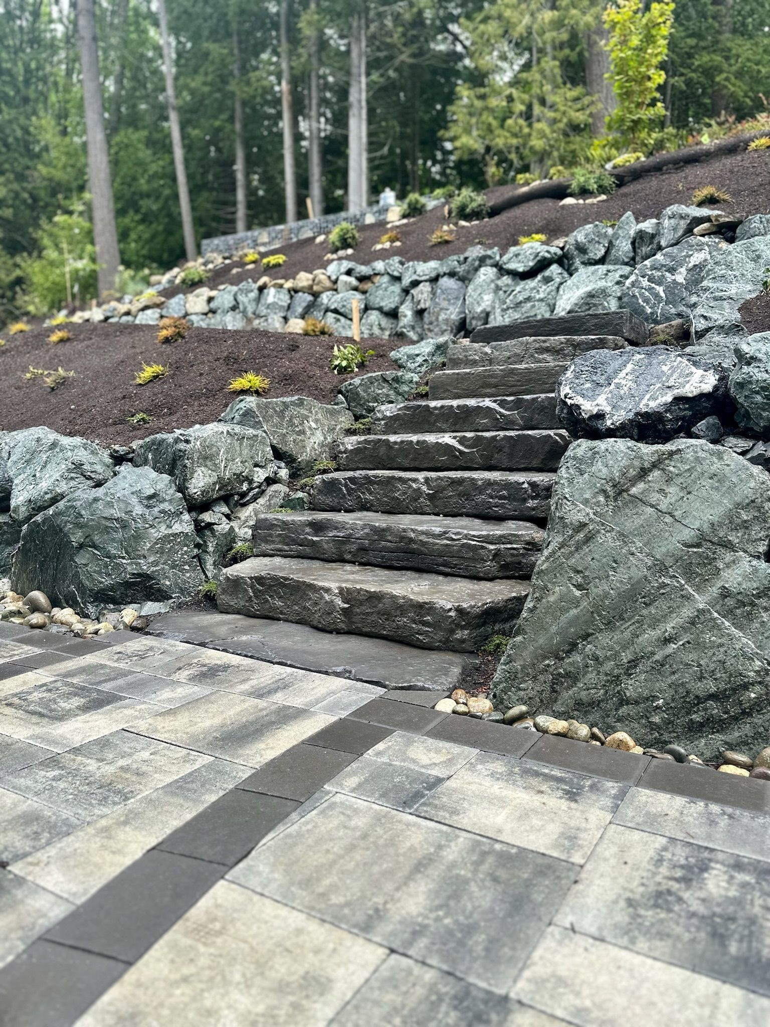 Stone steps ascend a terraced hillside with rock retaining walls and dark mulch.