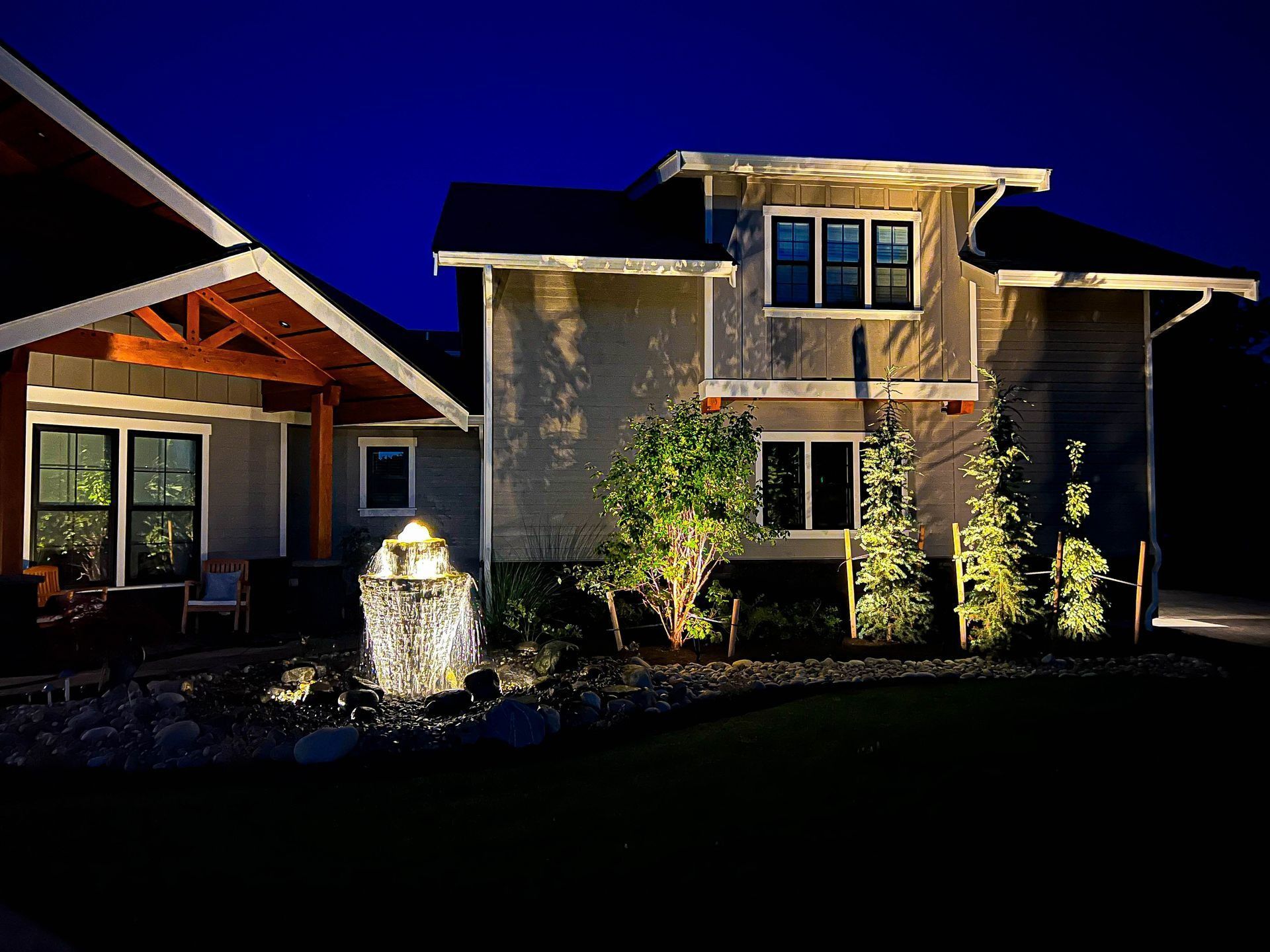 House exterior illuminated at night, featuring a lit fountain and landscaping.