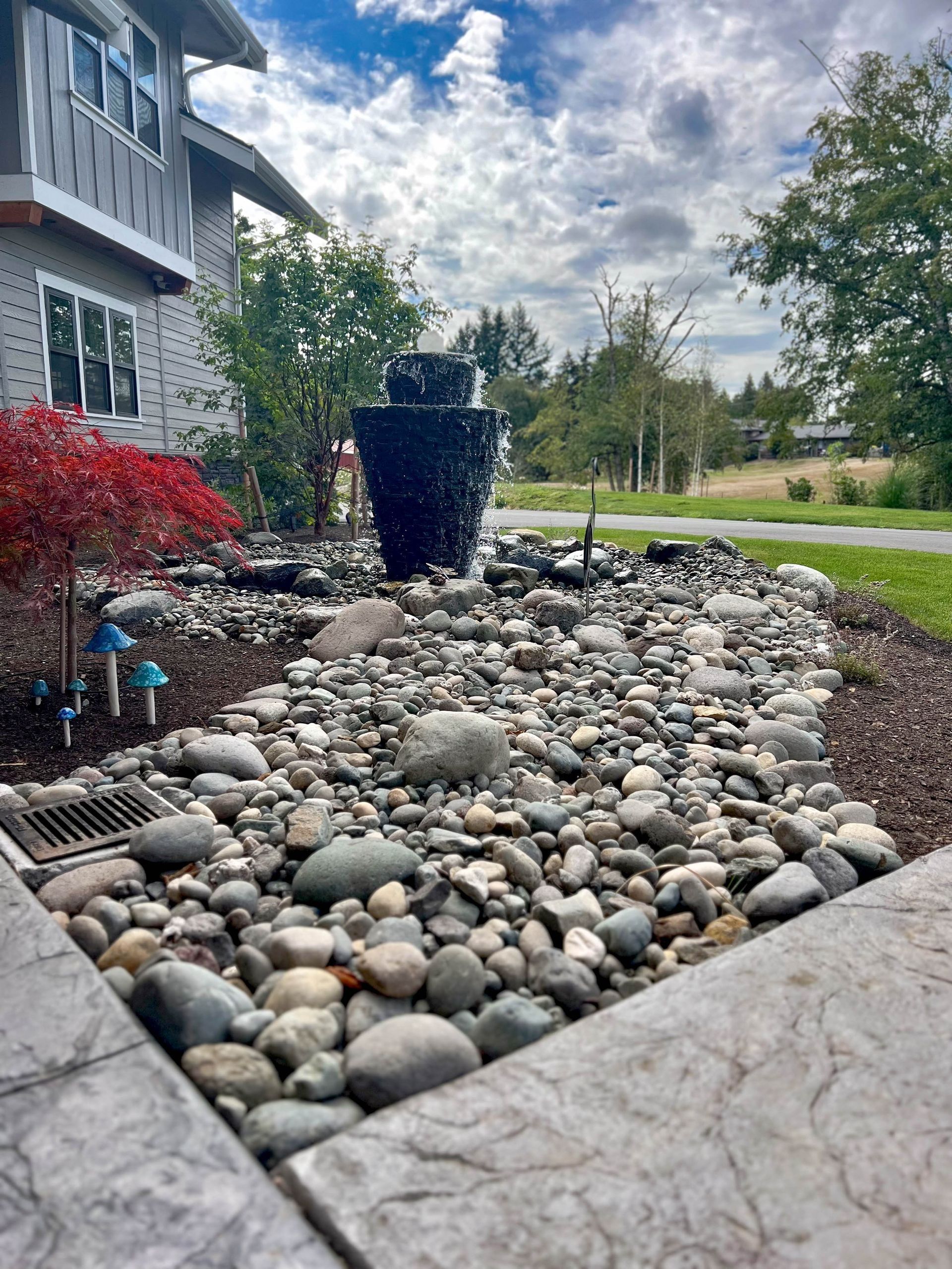 Landscaped yard with stone bed, fountain, and house in the background.