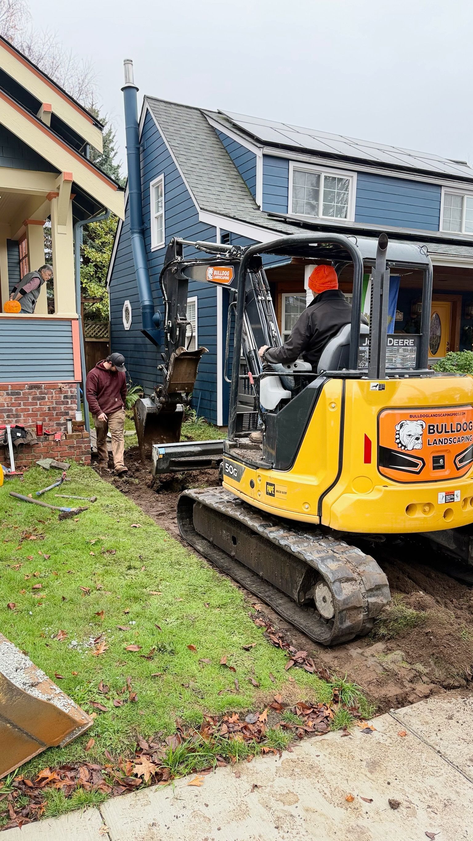 Yellow excavator digging beside a building with workers nearby on a grassy site