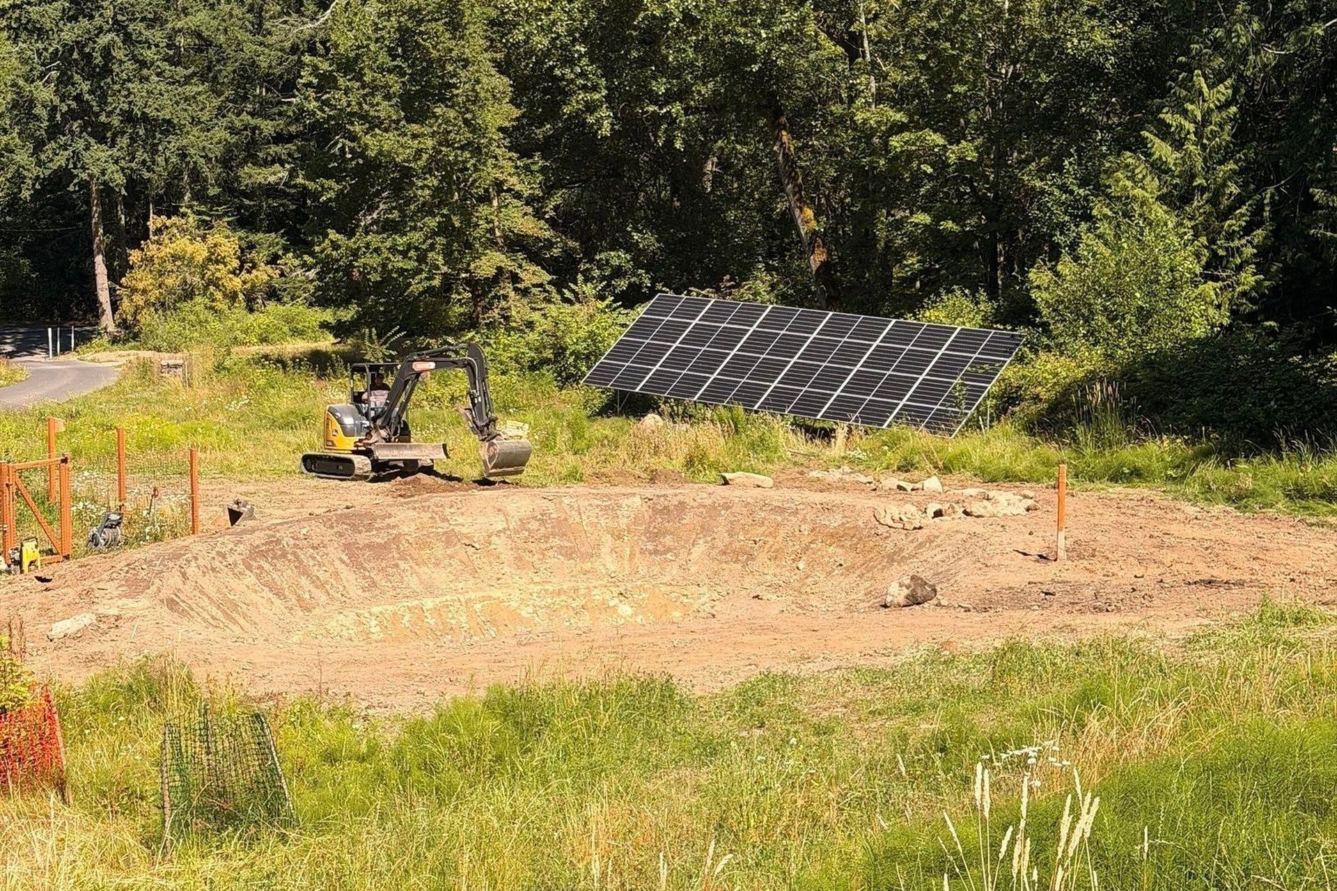Small garden plot with a compact excavator and a tilted solar panel in a grassy field by trees