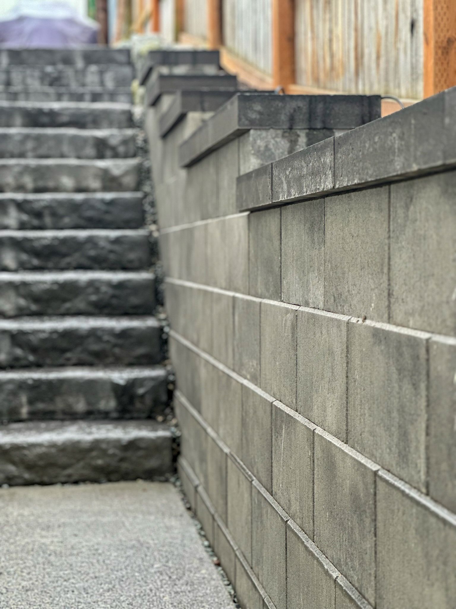 Concrete stairs beside a gray block retaining wall and wooden fence outdoors