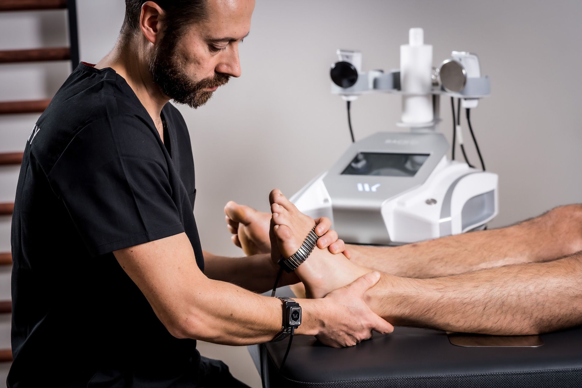 Woman administering TECAR treatment to a man's arm in a clinic setting.