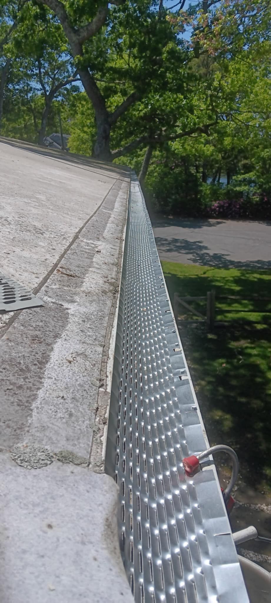 A close up of a metal gutter on a roof with trees in the background.