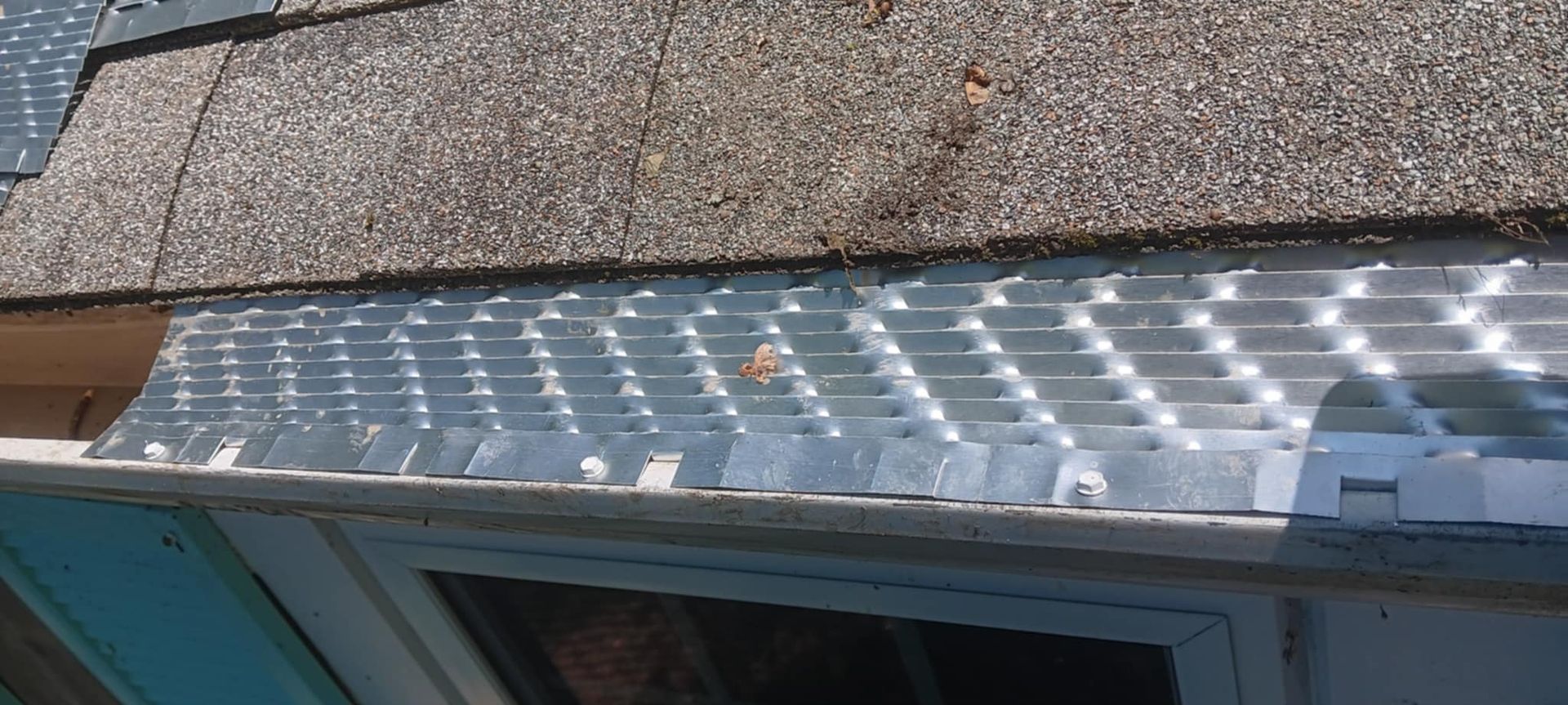 A close up of a gutter on a roof next to a window.