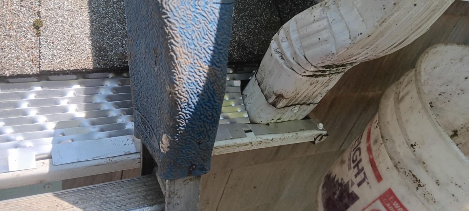 A person is working on a roof next to a bucket of paint.