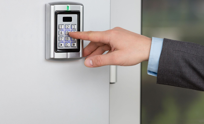 Hand entering a code on a keypad door lock, mounted on a white door.