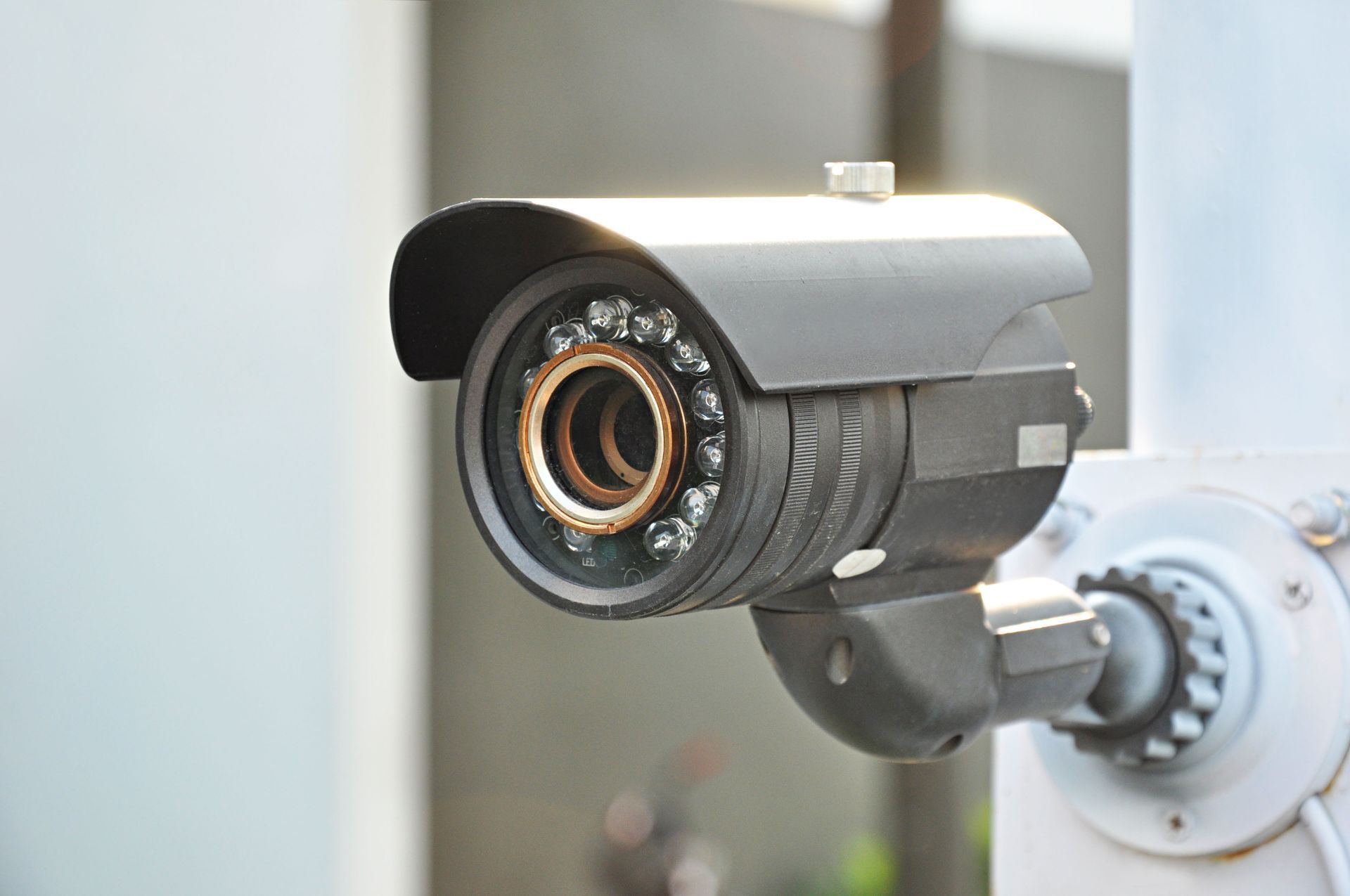 Black security camera mounted on a white pole, pointing forward.
