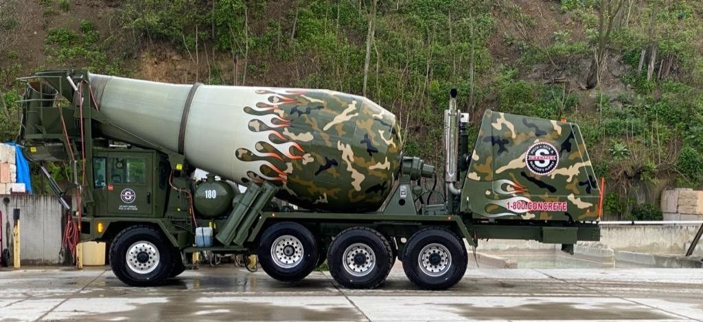 A camouflaged concrete mixer truck is parked on the side of the road.