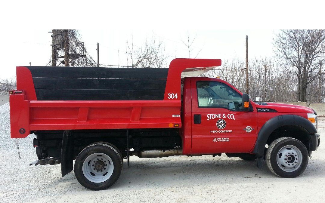 A red dump truck is parked on a gravel road