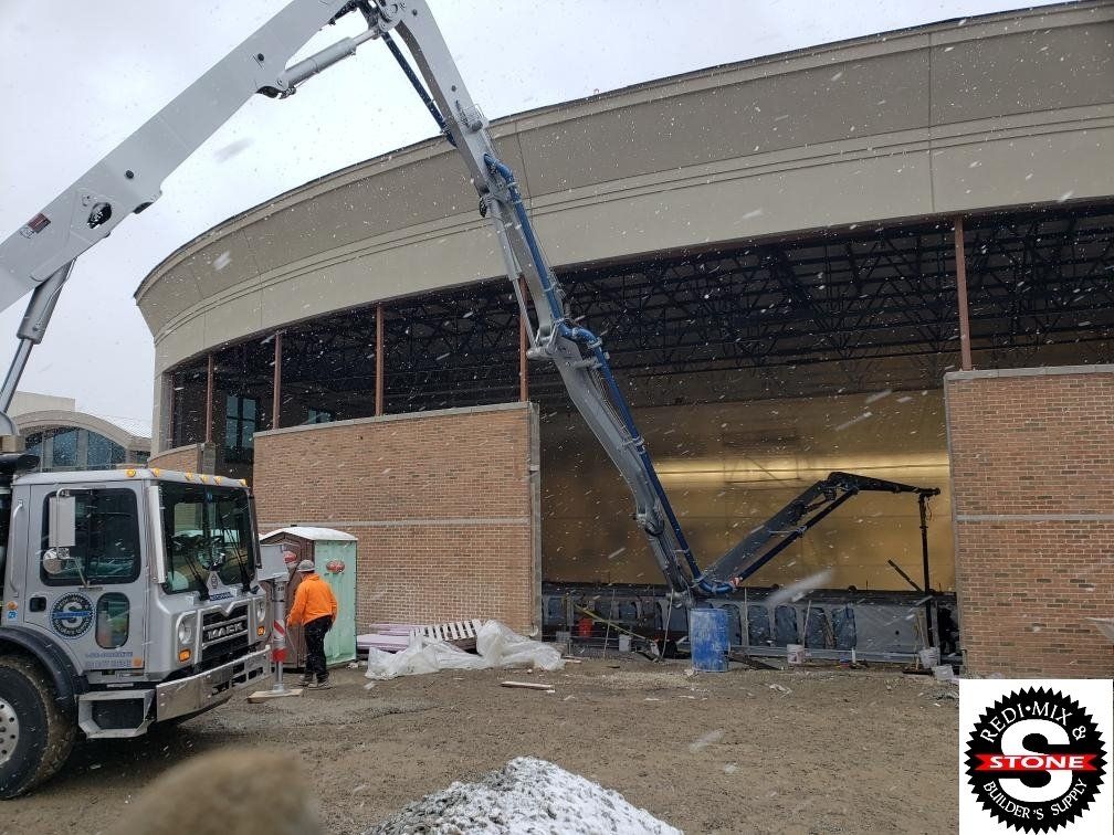 A white truck with a crane attached to it is parked in front of a building under construction.