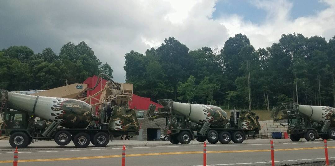 A row of concrete mixers are parked on the side of the road