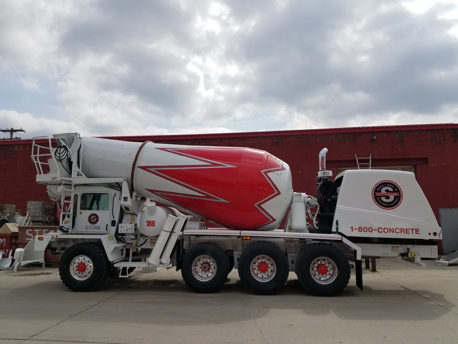A red and white concrete mixer truck is parked in front of a building