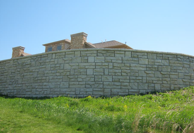 A large stone wall surrounds a grassy field with a house in the background