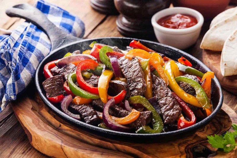 A pan filled with steak and peppers on a wooden table.