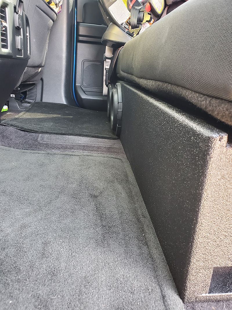 A subwoofer is sitting under a seat in a car