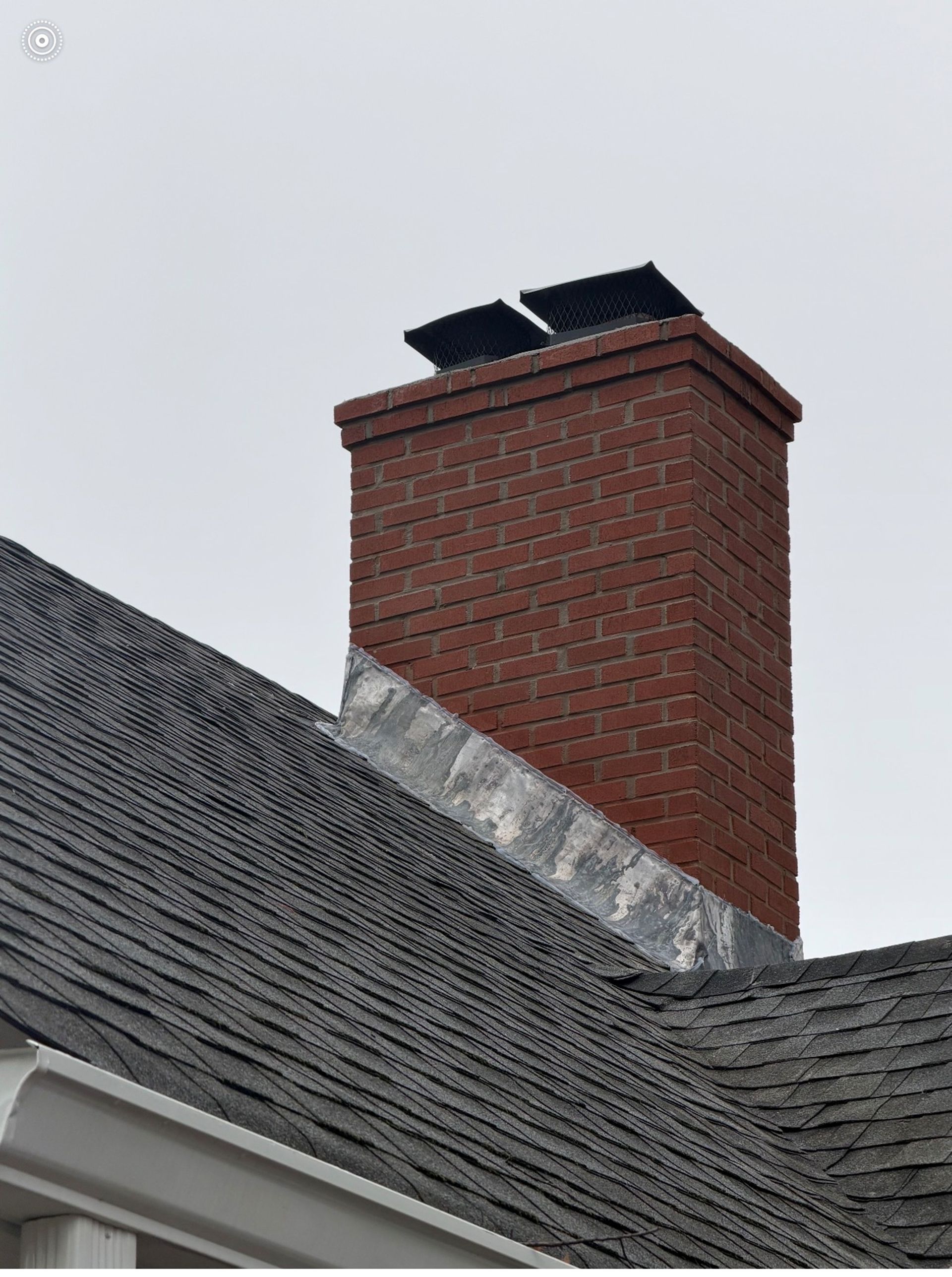 A brick chimney is sitting on top of a tiled roof.