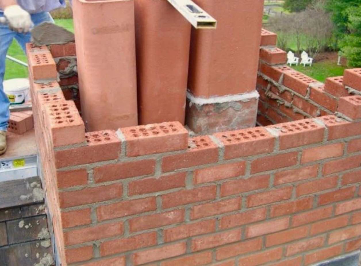 A man is laying bricks on top of a brick wall.