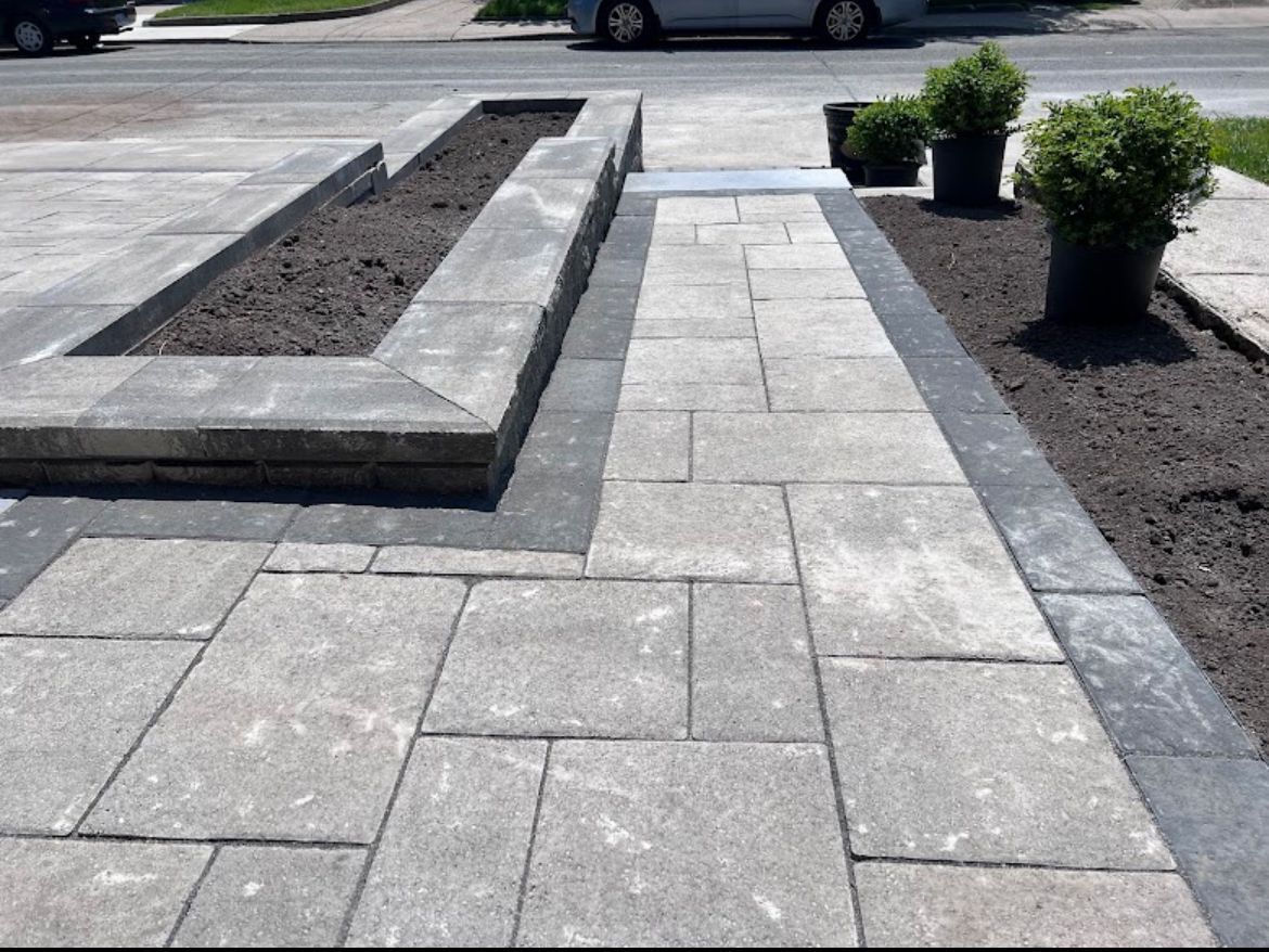 A brick walkway with planters and a car parked in the background