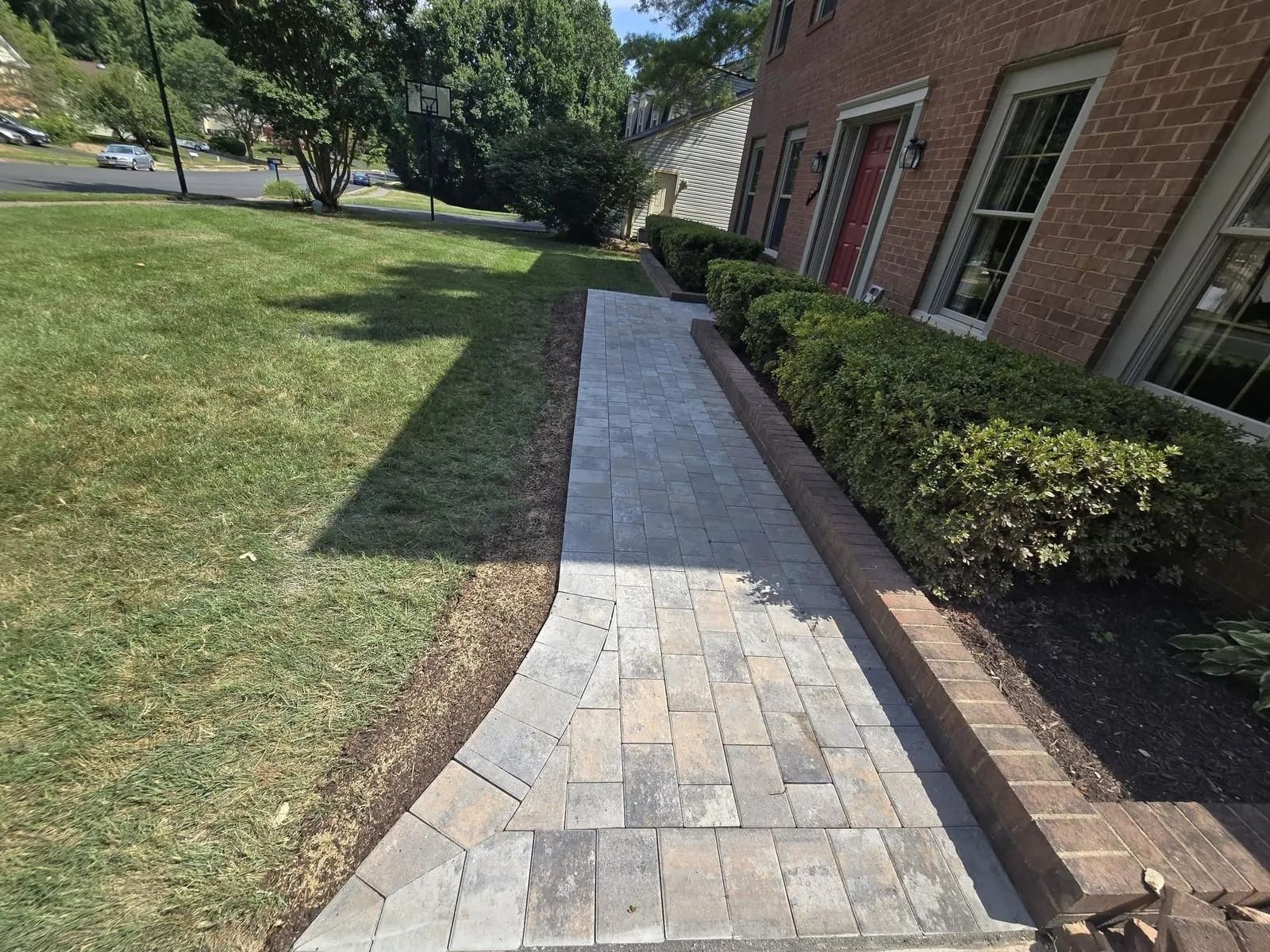 A brick walkway leading to a brick house with a red door