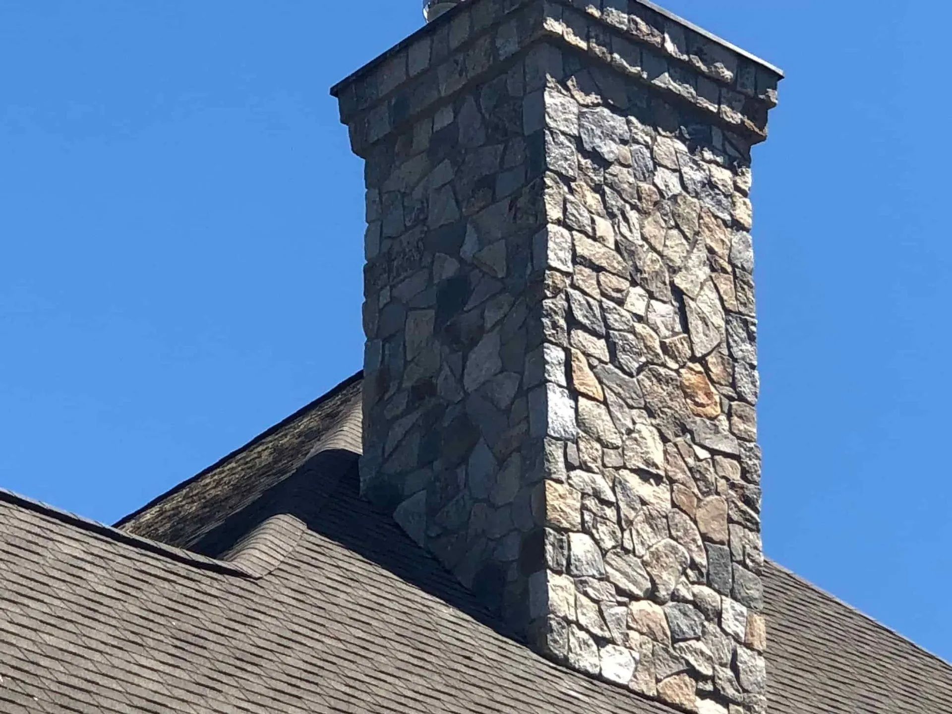 A stone chimney on top of a roof with a blue sky in the background