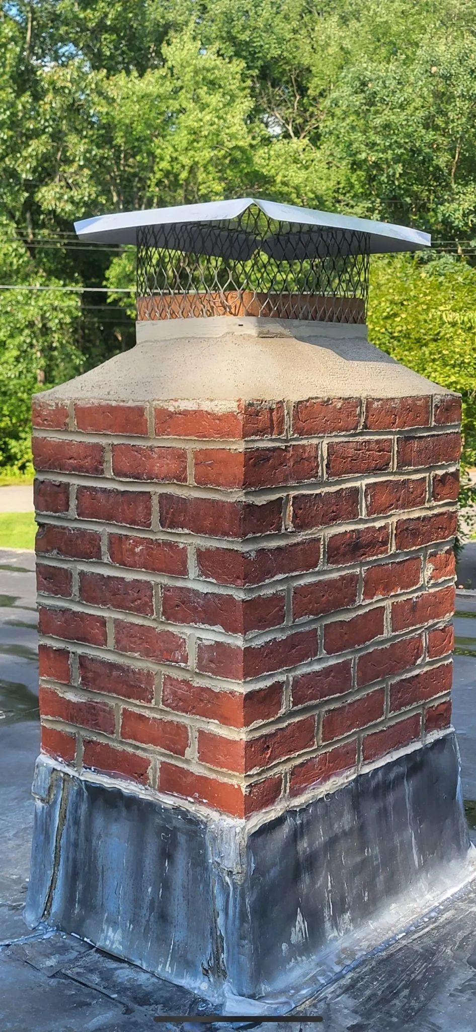 A brick chimney on top of a roof with trees in the background.