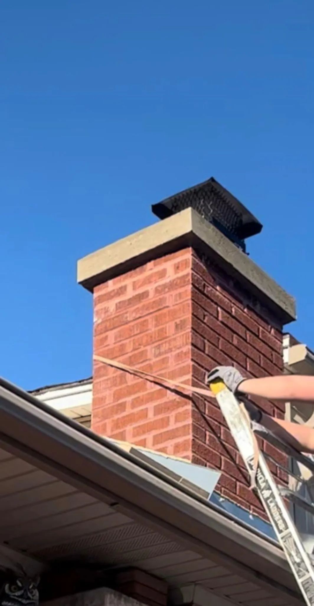 A person is standing on a ladder next to a brick chimney.