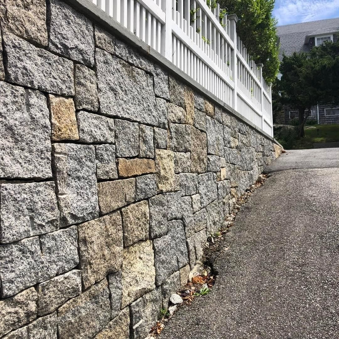A stone wall with a white fence along the side of it.