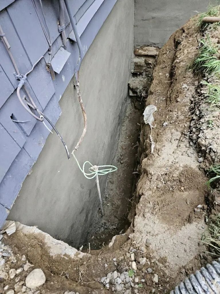 A hole in the ground next to a house with a hose coming out of it.