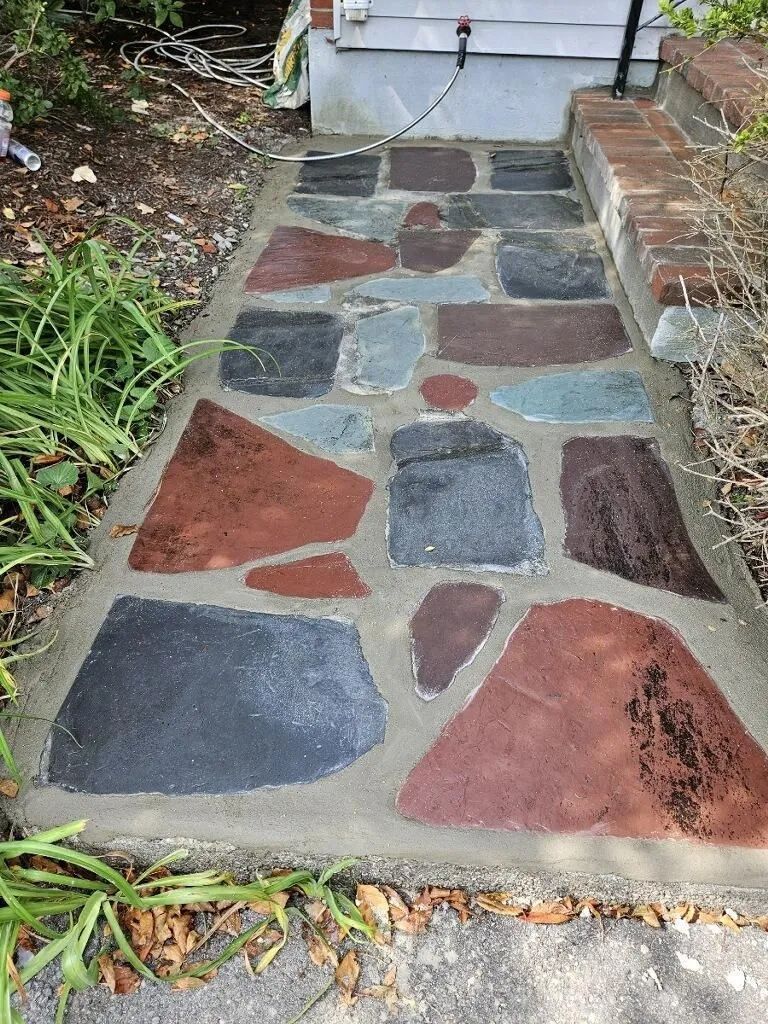 A stone walkway painted in different colors next to a house.