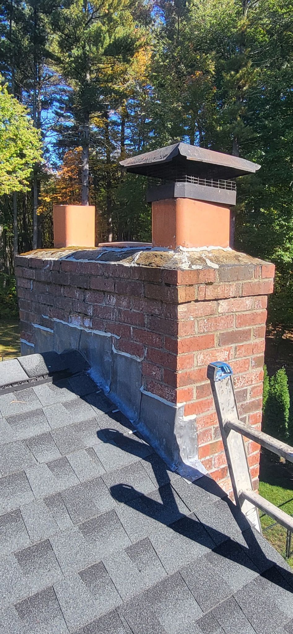 A brick chimney is sitting on top of a roof next to a ladder.