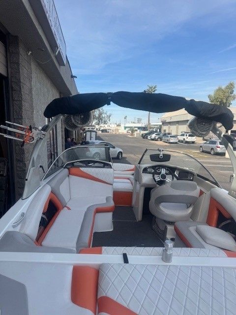 Interior of a white and orange boat with cushioned seating and a black bimini top, parked outside.