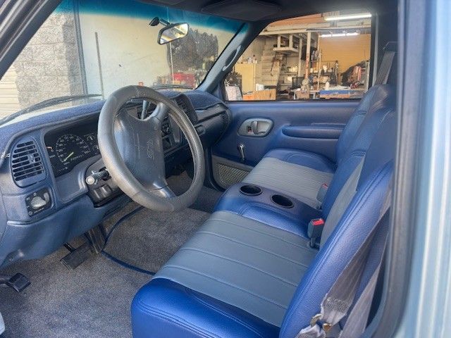 Interior of a blue Chevrolet pickup truck; blue seats, grey carpet, steering wheel, dashboard.