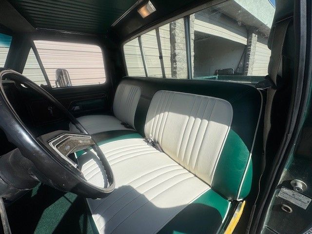 Interior of a vintage green truck with a white and green bench seat and black steering wheel.