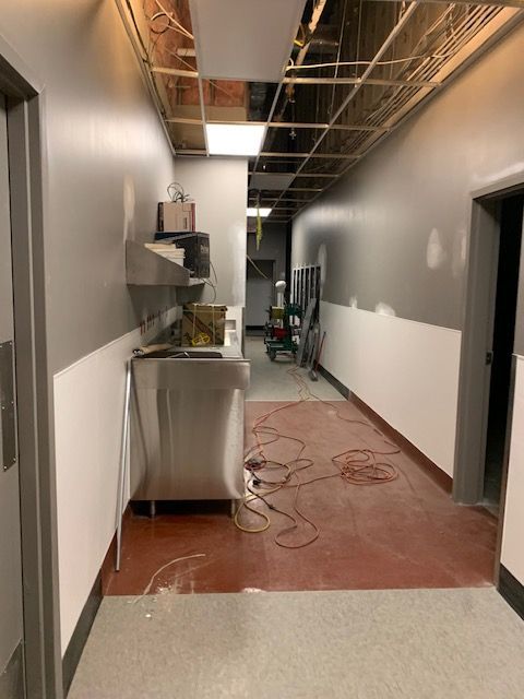 Hallway under construction, with gray and white walls, exposed ceiling, stainless steel sink.