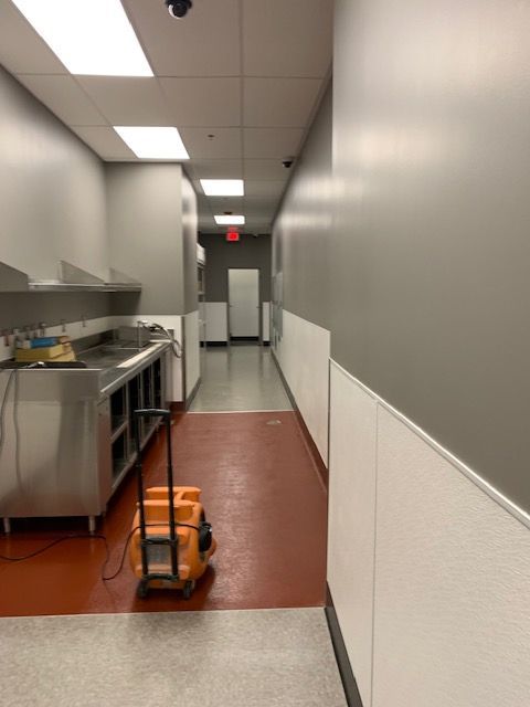 A narrow commercial kitchen hallway with gray walls, stainless steel counters, and a service cart.